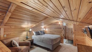 A cozy bedroom with a wooden ceiling, a bed, a nightstand, a lamp, and a chair. - "The Lodge"-  APT w/Loft Bedroom, Walnut Bar, Quiet Setting, Covered Parking (Enterprise)
