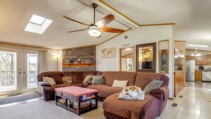 A living room with a brown sectional sofa, a ceiling fan, a skylight, and a kitchen in the background. - Sevierville Home: Lookout Deck, 10 Mi to Dollywood (Sevierville)