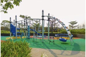 Explore the playground area with a climbing frame, slide, and swing set amidst lush surroundings.