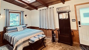 Ein Schlafzimmer mit Holzboden, einem Bett mit gemustertem Überwurf, einem Deckenventilator und einem Fenster mit Vorhängen.
