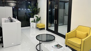 Una sala de estar moderna con una mesa de vidrio, un sillón amarillo y un armario blanco.