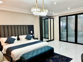 Un dormitorio moderno con una cama grande, un banco tapizado, una araña y un cerrojo corredizo que da a un baño.
