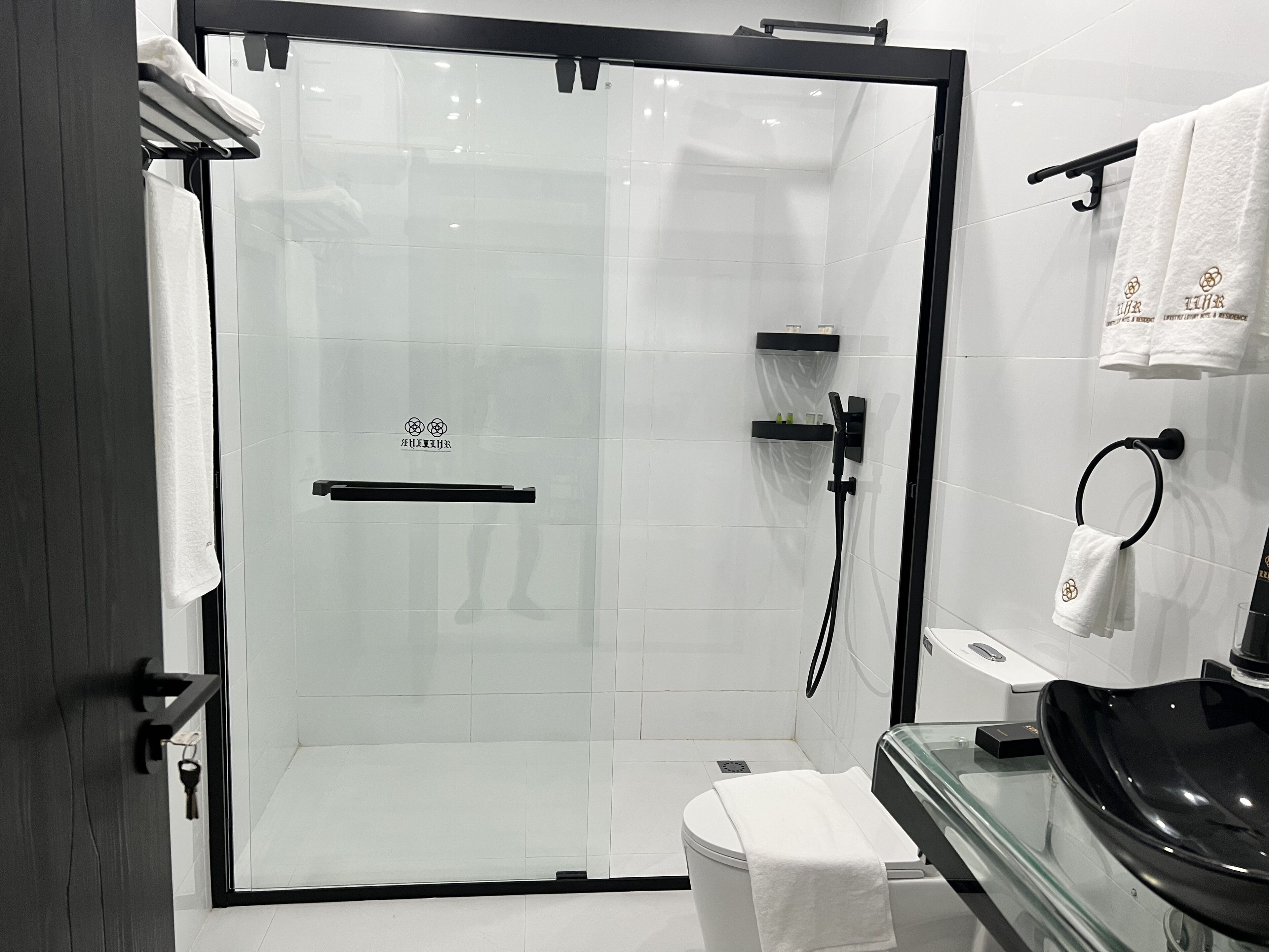 Une salle de bain moderne avec une douche à parois de verre, un lavabo noir et des carreaux blancs.