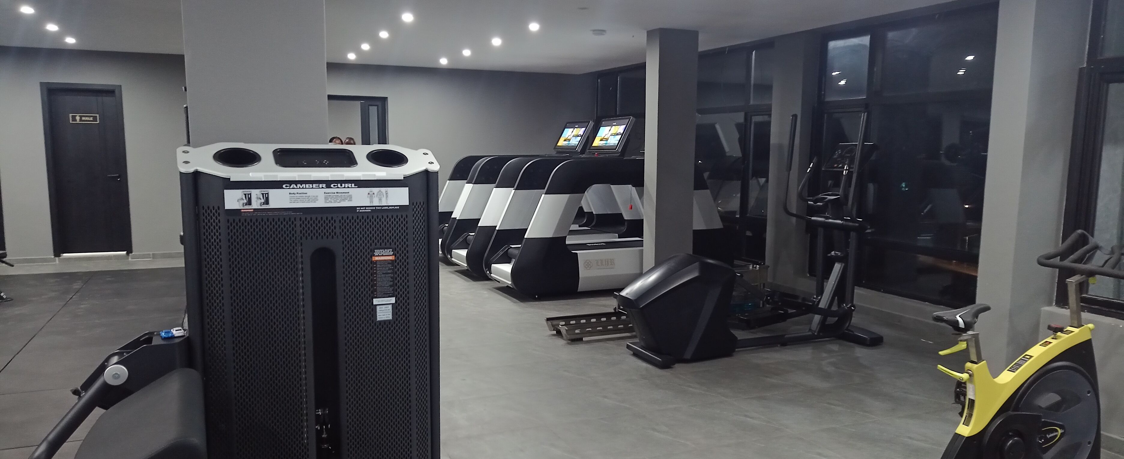 Een sportschool met loopbanden, een hometrainer en een machine voor bicep curls.
