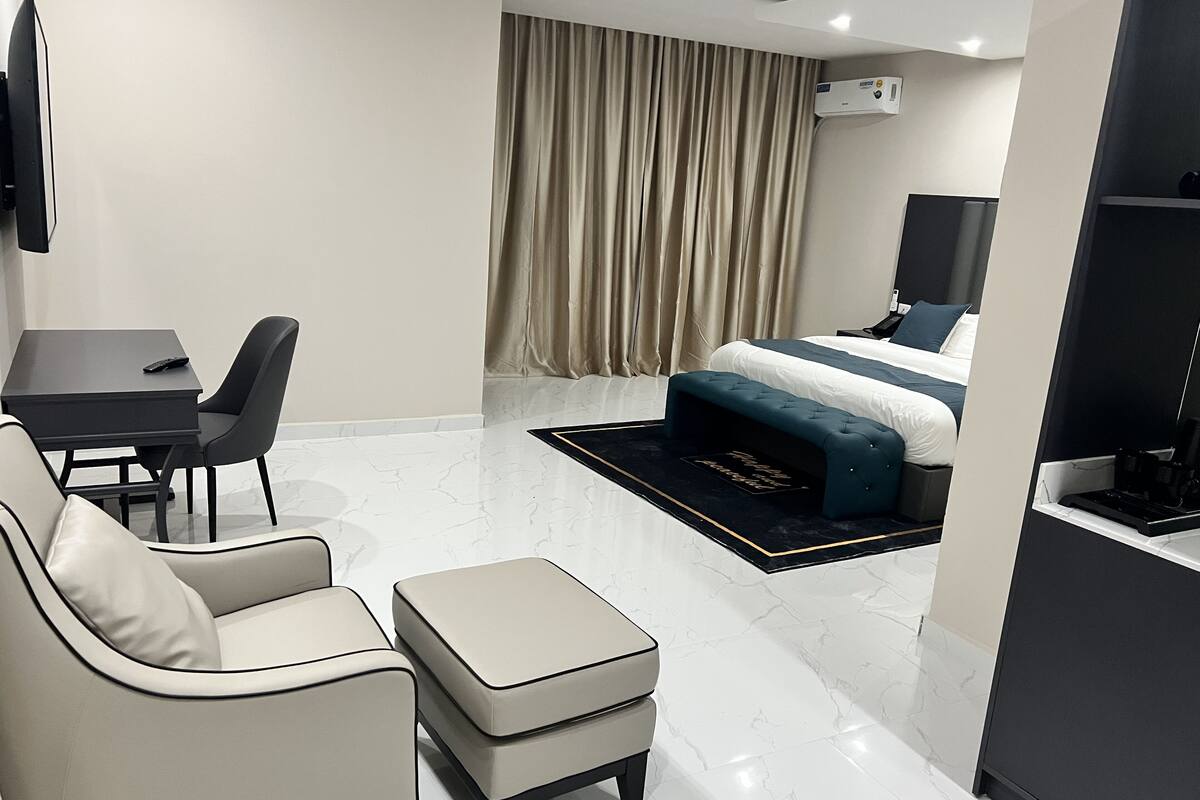 Een moderne hotelkamer met een bed, een bureau met stoel, een bank en een voetenbankje.