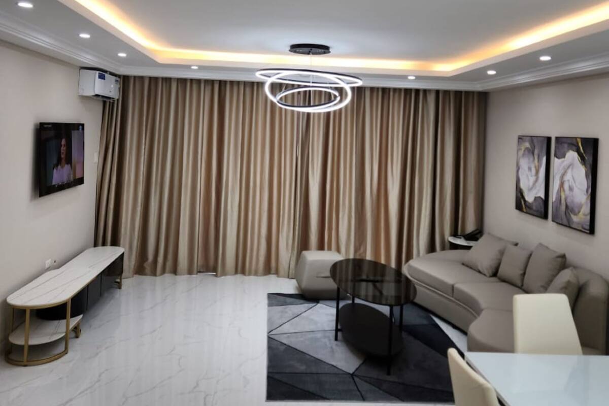 Een moderne woonkamer met een bank, een eettafel en een aan de muur bevestigde televisie.