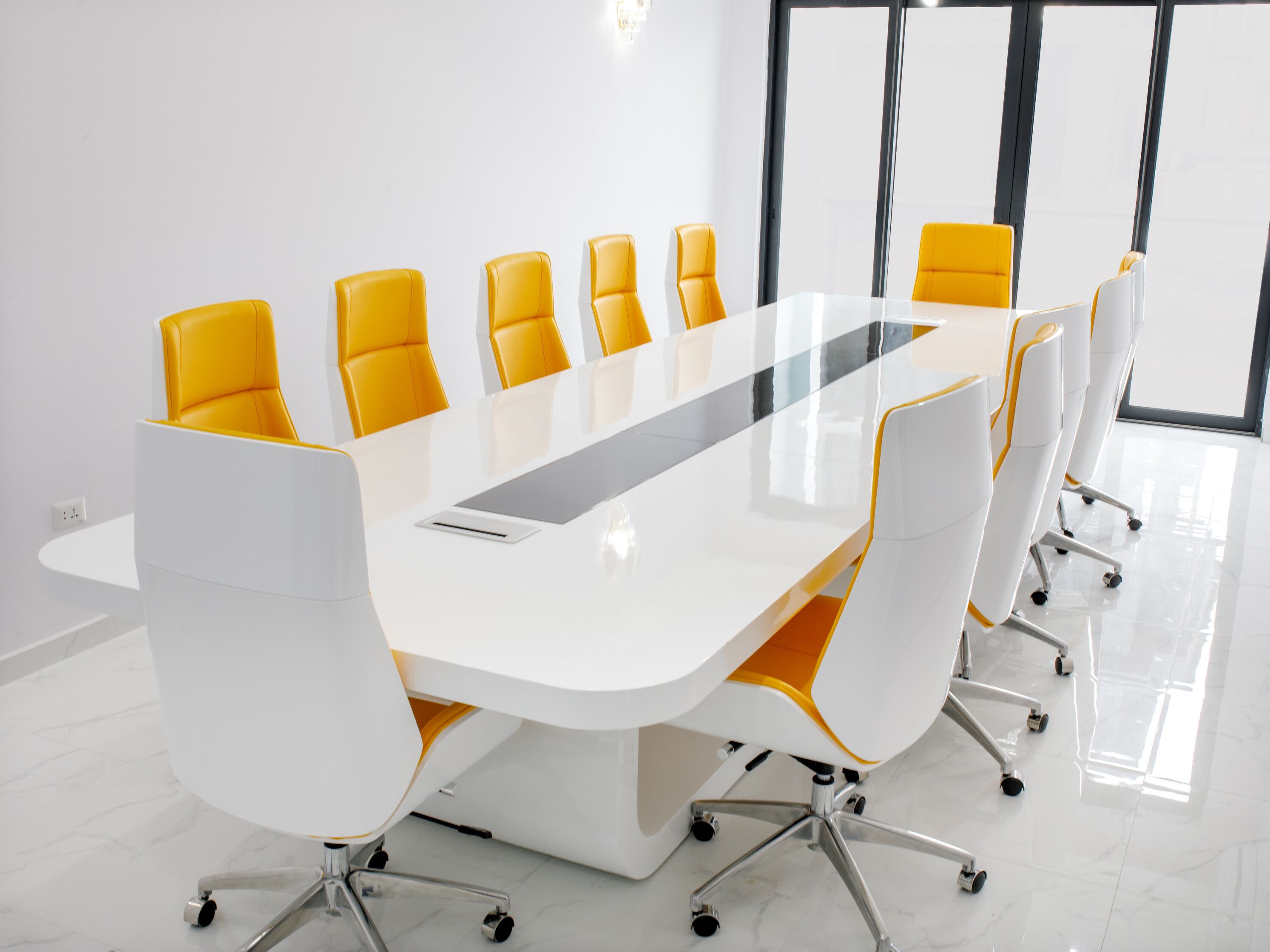 A conference room with a long white table and yellow chairs.