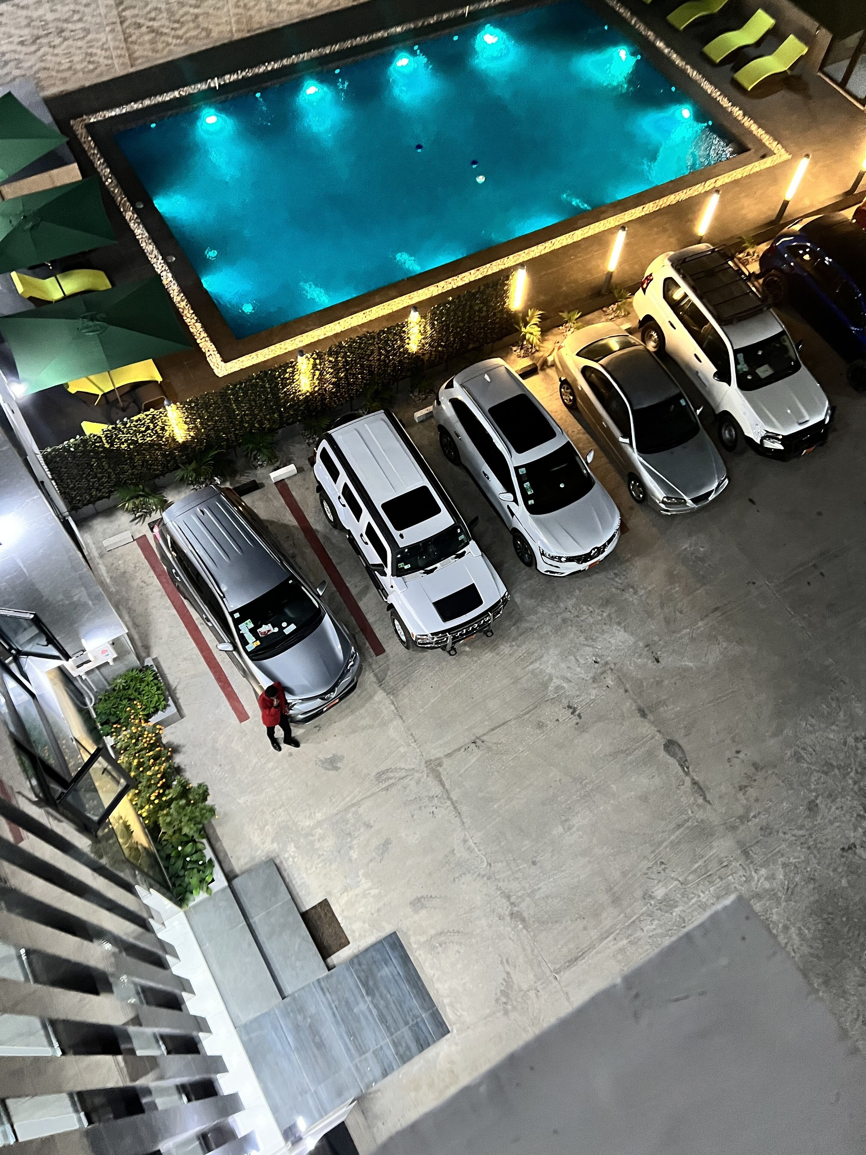 An aerial view of a parking area with a swimming pool, several cars, and a person walking.