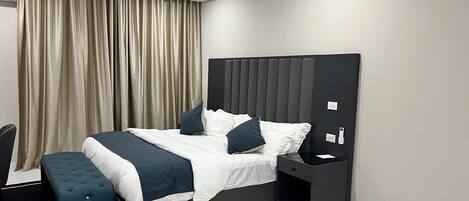 Una habitación de hotel moderna con una cama grande, una mesita de noche, una silla y una cortina.