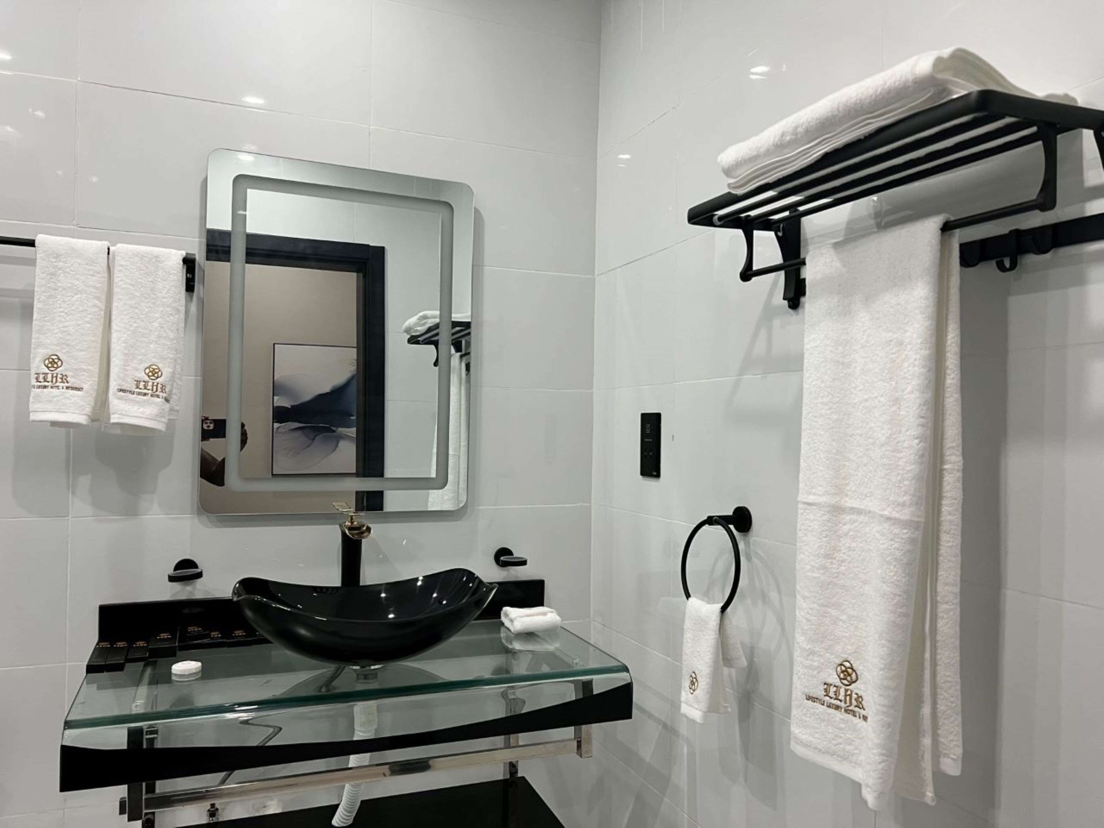 A modern bathroom with a glass sink, a black vessel sink, a large mirror, and white tiled walls.