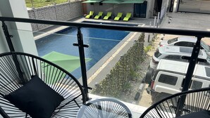 Un balcón con dos sillas y una mesita, con vista a una piscina y un estacionamiento con coches.