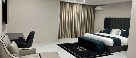 Quarto de hotel moderno com uma cama grande, uma escrivaninha, uma cadeira e uma televisão de tela plana.