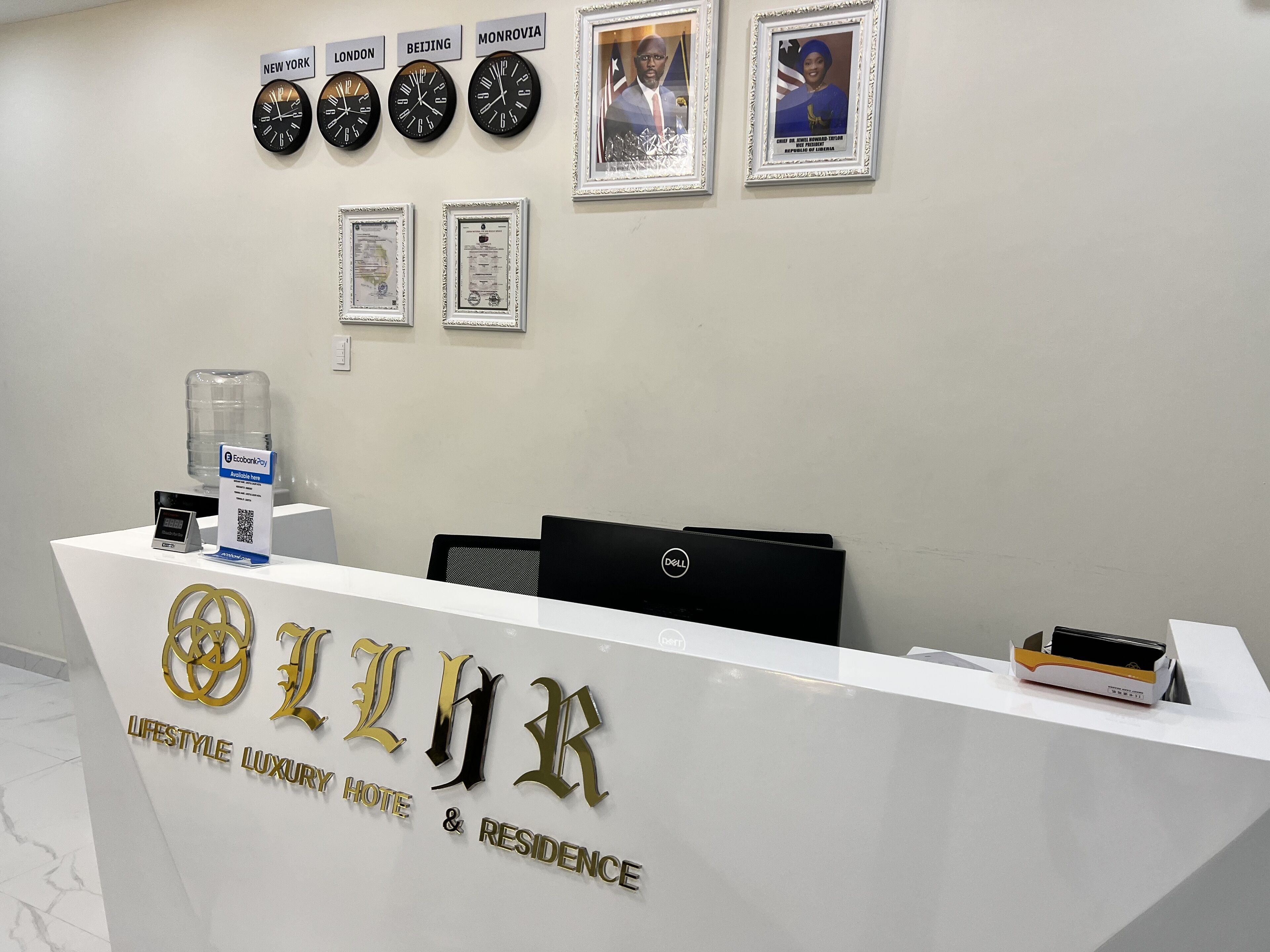A reception desk with clocks showing New York, London, Beijing, and Monrovia times, framed certificates, and a Dell computer.