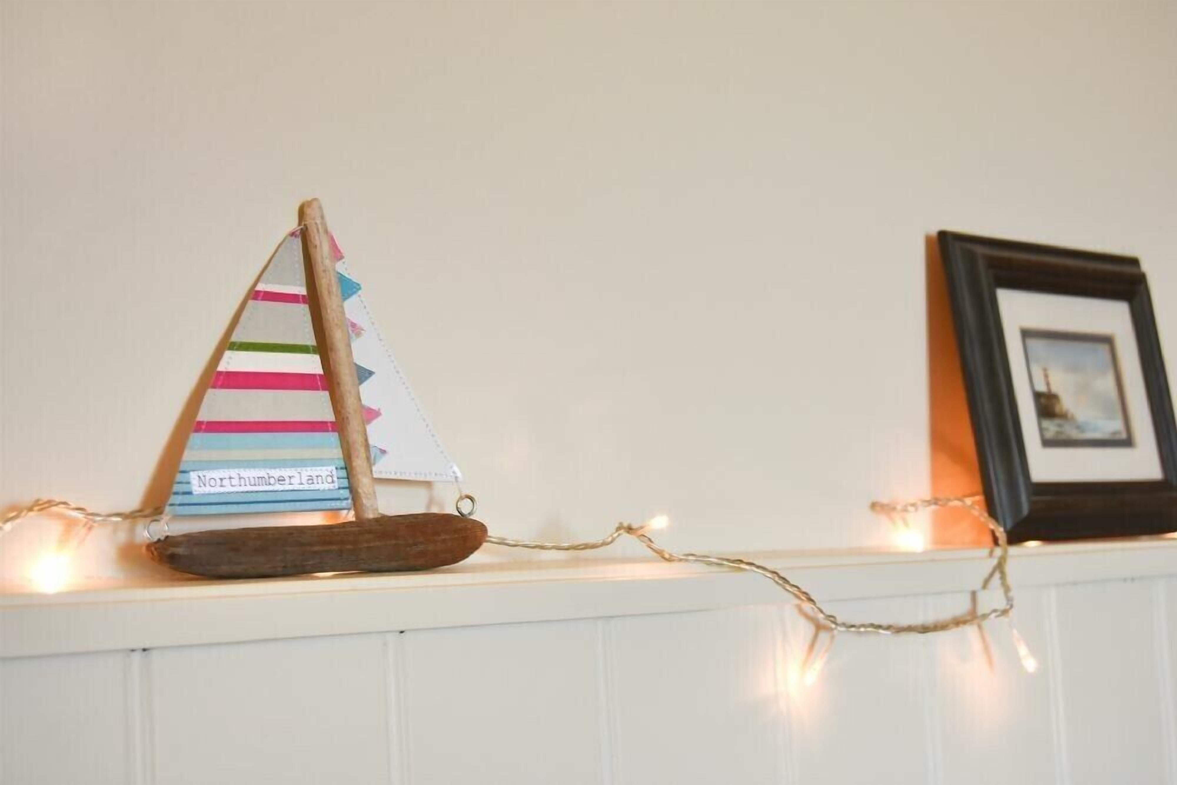 Un velero decorativo con vela a rayas y base de madera sobre una repisa.