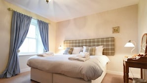 A double bed with a plaid headboard, two bedside lamps, and a small table with a bowl.