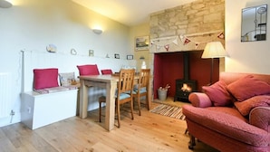 A cozy living room with a stone fireplace, a wooden dining table with chairs, a red sofa, and a white bench with cushions.