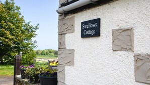 En skylt med texten ”Swallows Cottage” sitter på en vit vägg, och i bakgrunden syns en trädgård.
