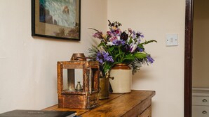 En hylla i trä med en rustik lykta, en vas med blommor och en inramad tavla.