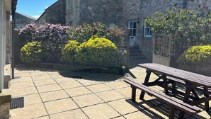 A stone building with a tiled patio and a wooden bench. - Beachward (Alnwick)