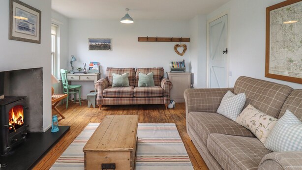 A cozy living room with a fireplace, two couches, a wooden coffee table, and a desk with a lamp. - Beachward (Alnwick)
