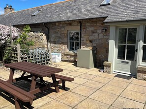 A stone building with a tiled patio, a wooden picnic table, and a door with glass panels.
