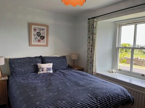 A bedroom with a bed, a nightstand, a lamp, a framed picture on the wall, and a window with curtains.