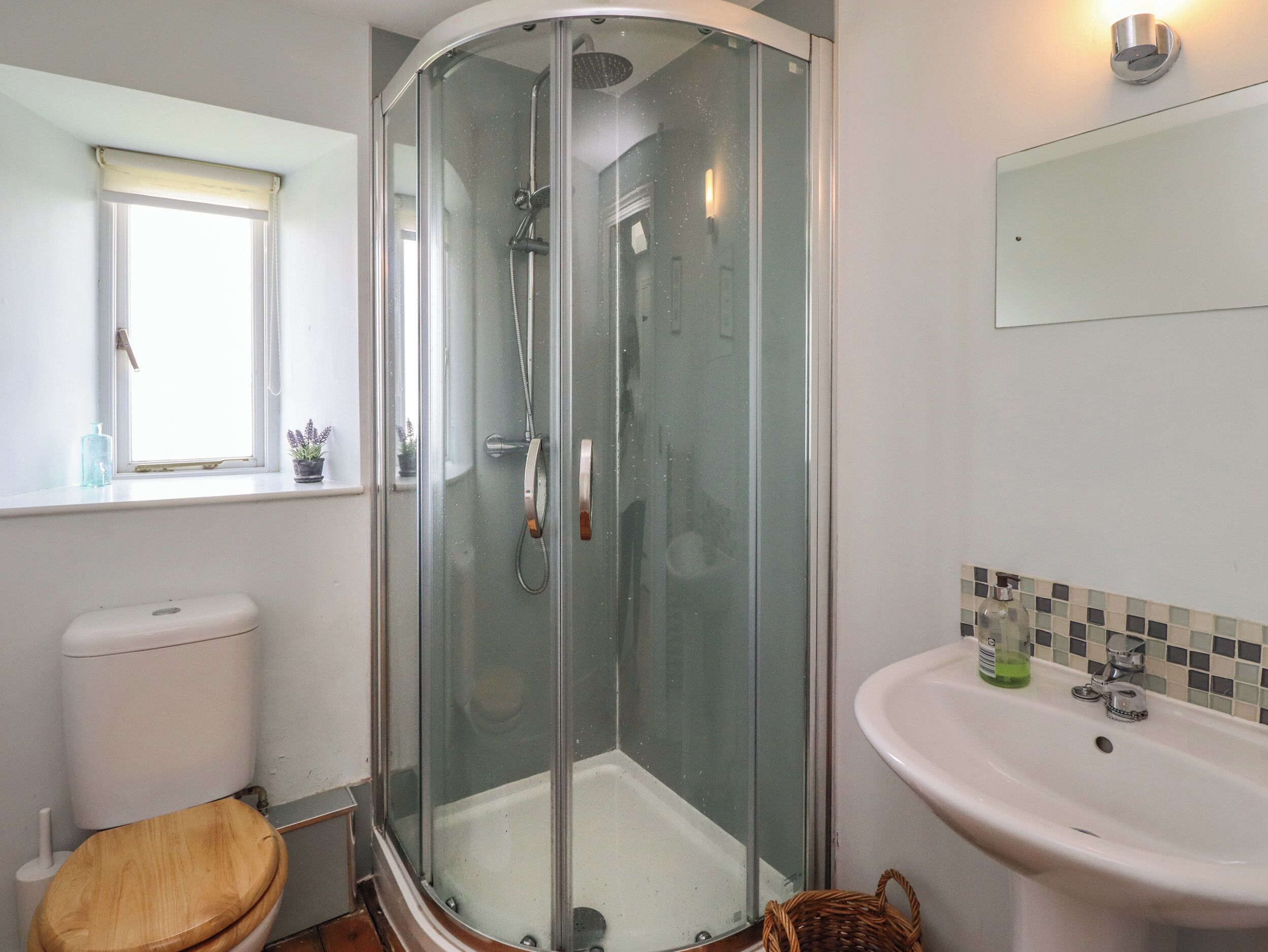 A bathroom with a glass-enclosed shower, a toilet, a sink, and a window.