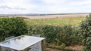 Ein Tisch mit Stühlen in einem Garten mit Blick auf einen Fluss und weite Hügel.