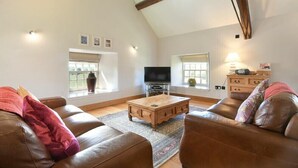 A spacious living room with a high ceiling, a wooden coffee table, leather sofas, and a television. - Budle Sands (Bamburgh)