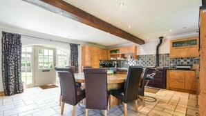 A kitchen with wooden cabinets, a tiled backsplash, and a dining area with a table and chairs. - Budle Sands (Bamburgh)