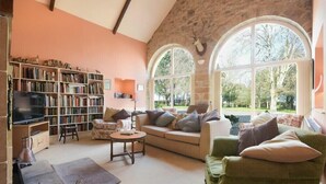 A cozy living room with a fireplace, bookshelves, and a large window with a view of trees.