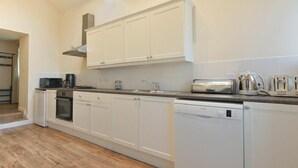 A modern kitchen with white cabinets, a built-in oven, a dishwasher, and a coffee maker. - Stewart House (Wooler)