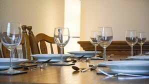 A dining table set with wine glasses, plates, and cutlery, with a wooden chair and a lamp in the background. - Stewart House (Wooler)
