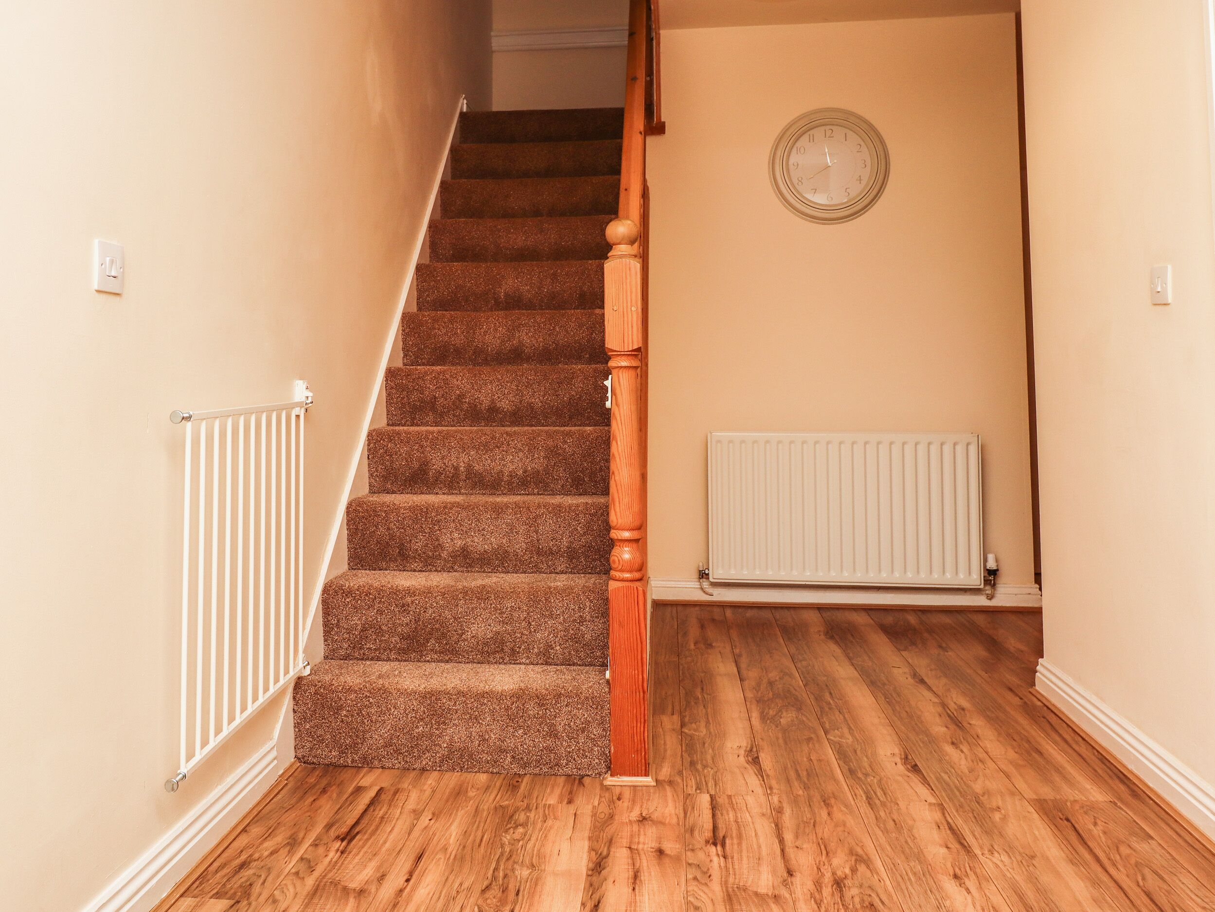 A wooden staircase with carpeted steps, a white radiator, and a wall-mounted clock.