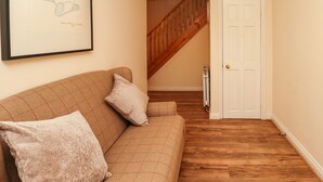 A living room with a brown sofa, two pillows, a framed picture on the wall, a wooden staircase, and a white door. - Stewart House (Wooler)