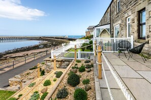 A coastal building with a stone facade, a white fence, and a patio area with outdoor seating. - Old Coastguard Cottages (Morpeth)