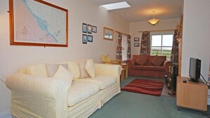 A living room with a sofa, a red armchair, a television, and a map on the wall. - Snook Point Cottage (Alnwick)