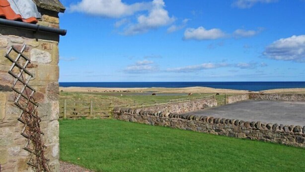 A stone building with a grassy yard and a view of the sea. - Snook Point Cottage (Alnwick)