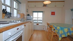 A kitchen with a stove, sink, and window. There is a table with a tablecloth and chairs. - Snook Point Cottage (Alnwick)