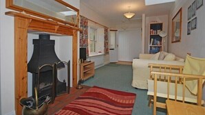 A cozy living room with a fireplace, a sofa, a wooden crib, and a bookshelf. - Snook Point Cottage (Alnwick)