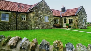 A stone building with a red-tiled roof, a grassy lawn, and a stone wall in the foreground. - Snook Point Cottage (Alnwick)