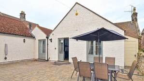 Ein weißes Gebäude mit einem Ziegeldach, einer Terrasse mit Tisch und Stühlen sowie einem schwarzen Sonnenschirm.