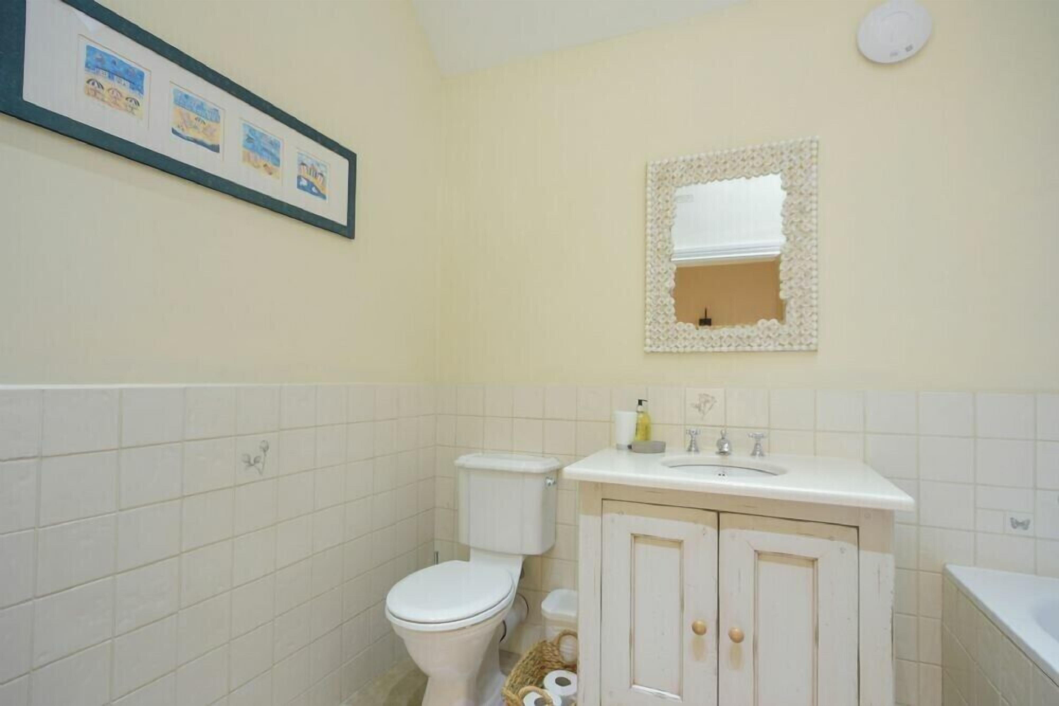 Een badkamer met toilet, wastafel en spiegel. Er hangt een lijst aan de muur en er staat een mand met broodjes op de vloer.