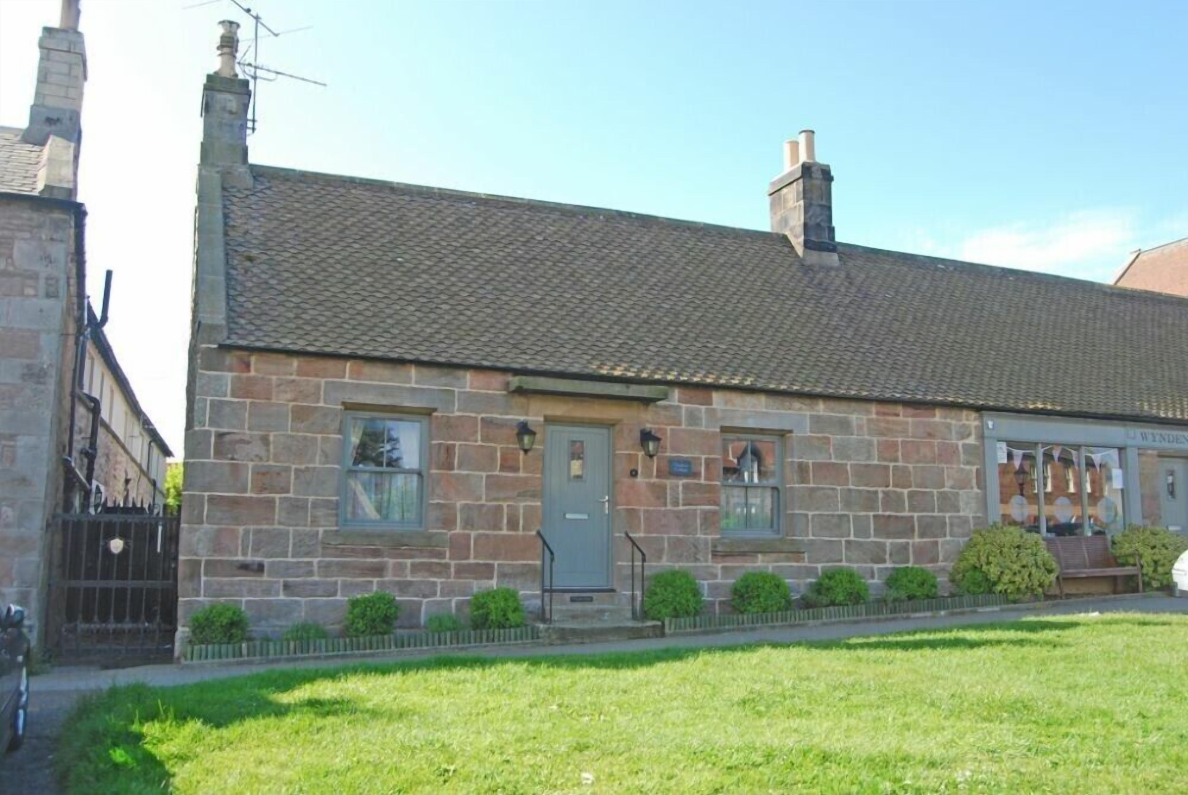 A stone building with a tiled roof, a front door, and a small porch area.