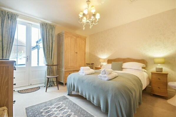 A bedroom with a large bed, a wooden wardrobe, a nightstand, a chair, and a chandelier. - Charlton Cottage (Bamburgh)