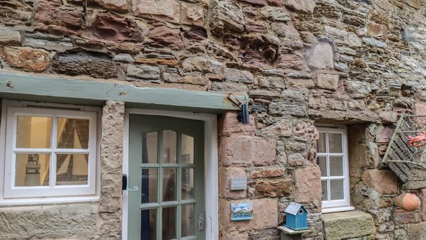 A stone building with a green door and windows. There is a birdhouse on the wall and a sign that reads "The Hotel". - The Little Boathouse (Seahouses)