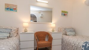A bedroom with two beds, a chair, and a mirror. - The Little Boathouse (Seahouses)