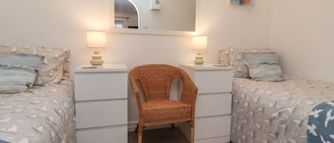 A bedroom with two beds, a chair, and a mirror.