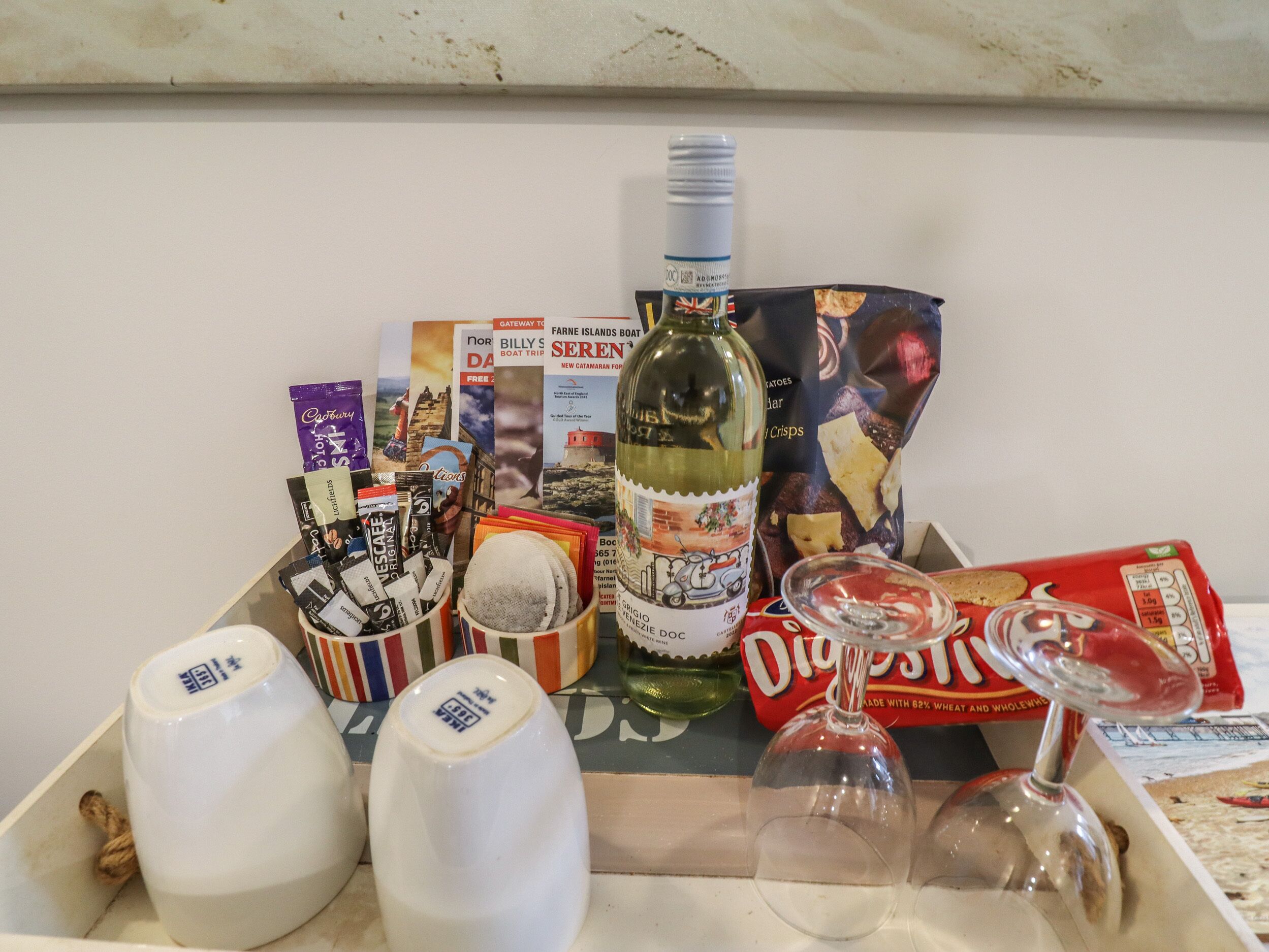 A tray with various items including a bottle of wine, wine glasses, a box of digestive biscuits, and some travel brochures.