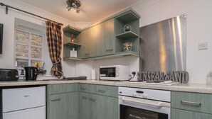 A kitchen with green cabinets, a white refrigerator, a microwave, and a stainless steel refrigerator. - The Little Boathouse (Seahouses)